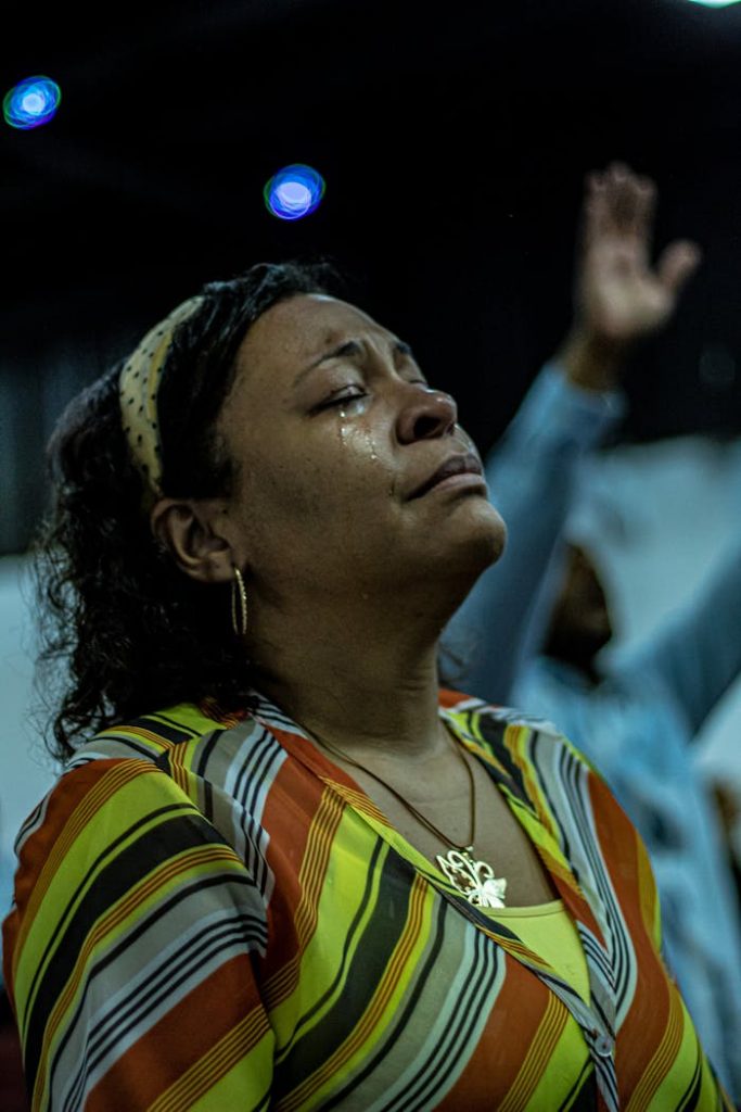 Woman shedding tears during a heartfelt moment of prayer indoors, in a spiritual setting.